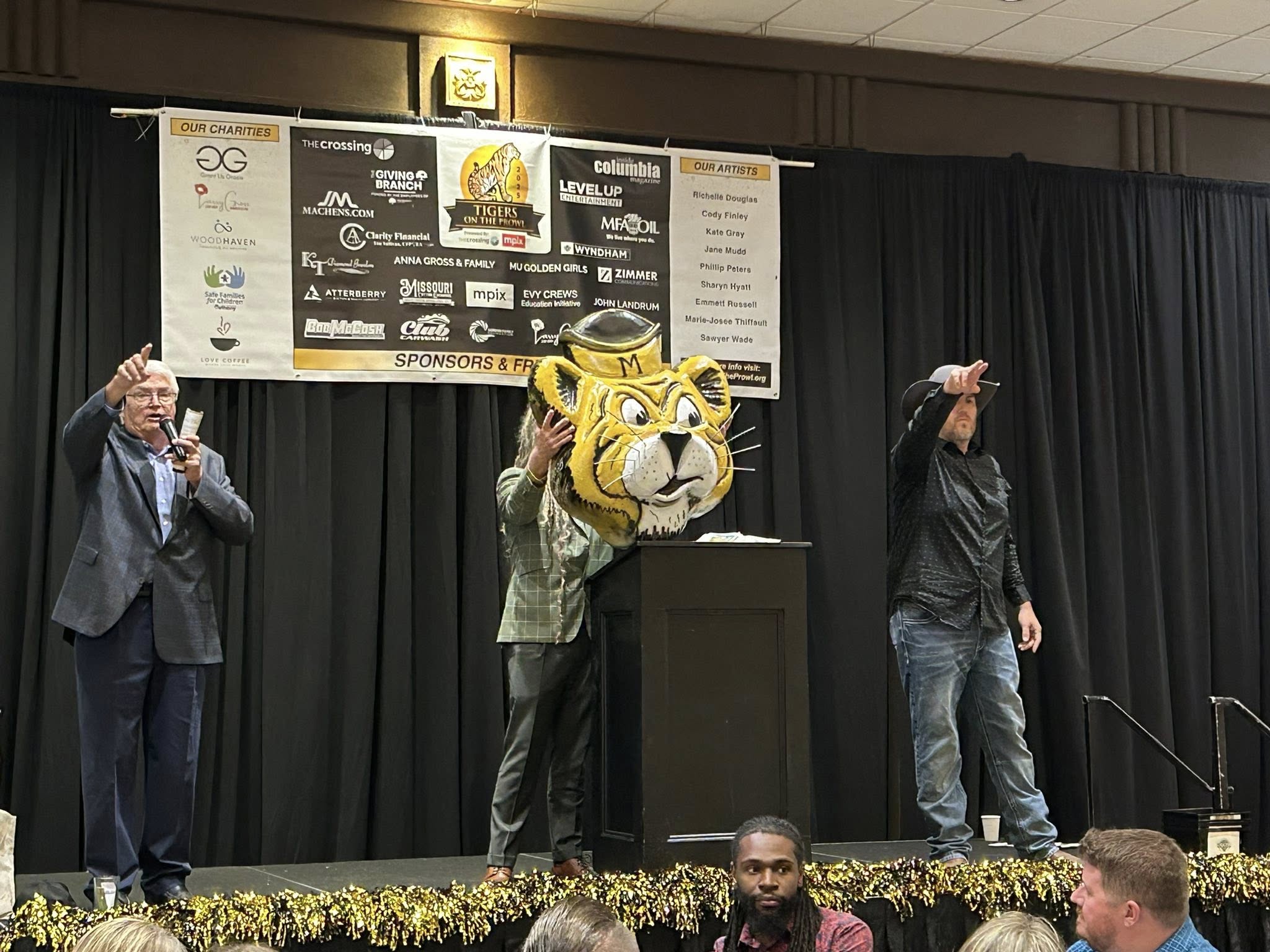 Tigers on the Prowl gala stage with emcee, Truman the Tiger mascot, and sponsors banner